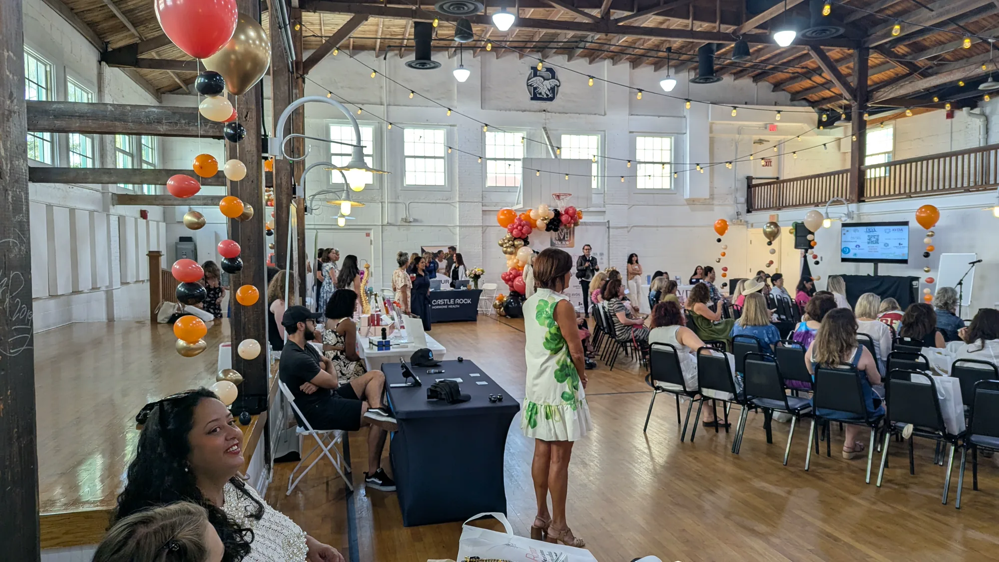 Audience, vendor tables, video display, and AV setup inside the Vintage Gym at Old School Square