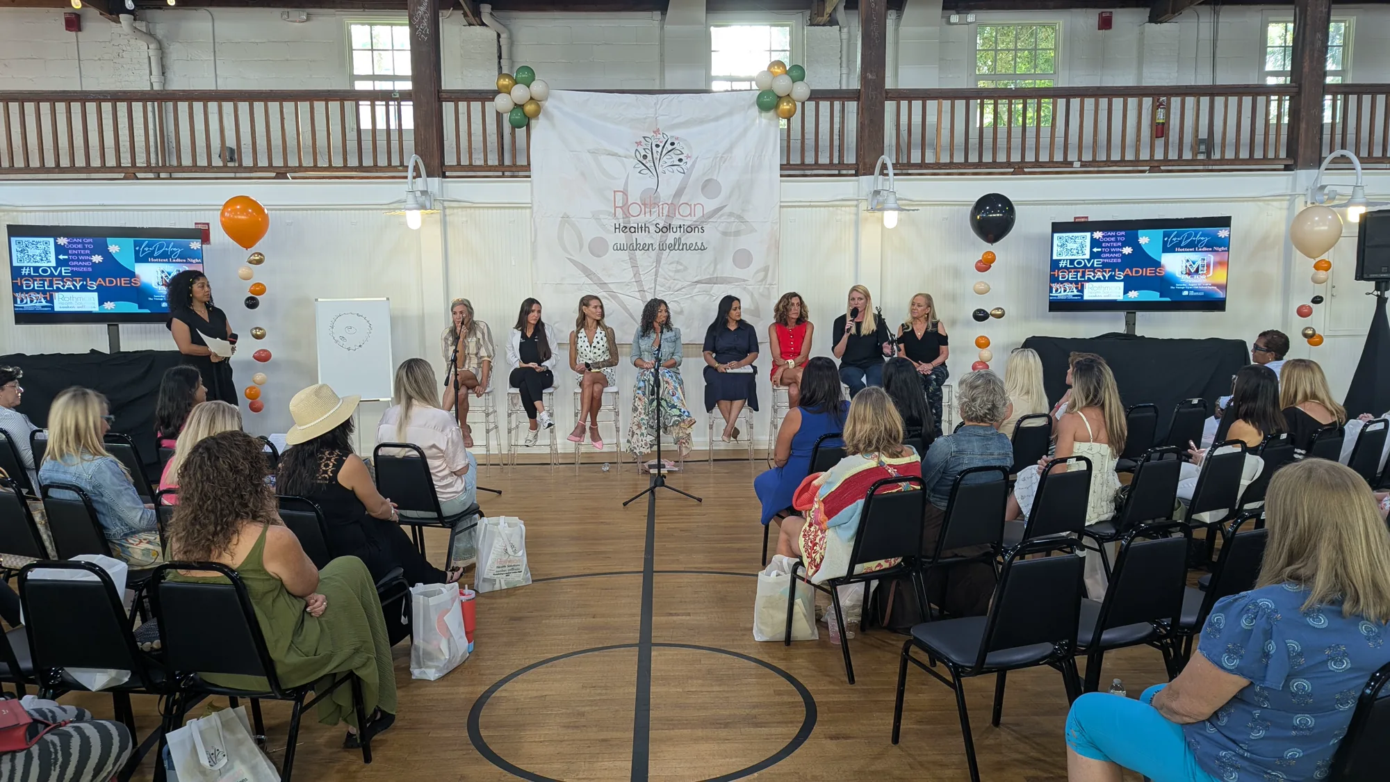 Women’s wellness panel seated on stage with microphones and two video displays