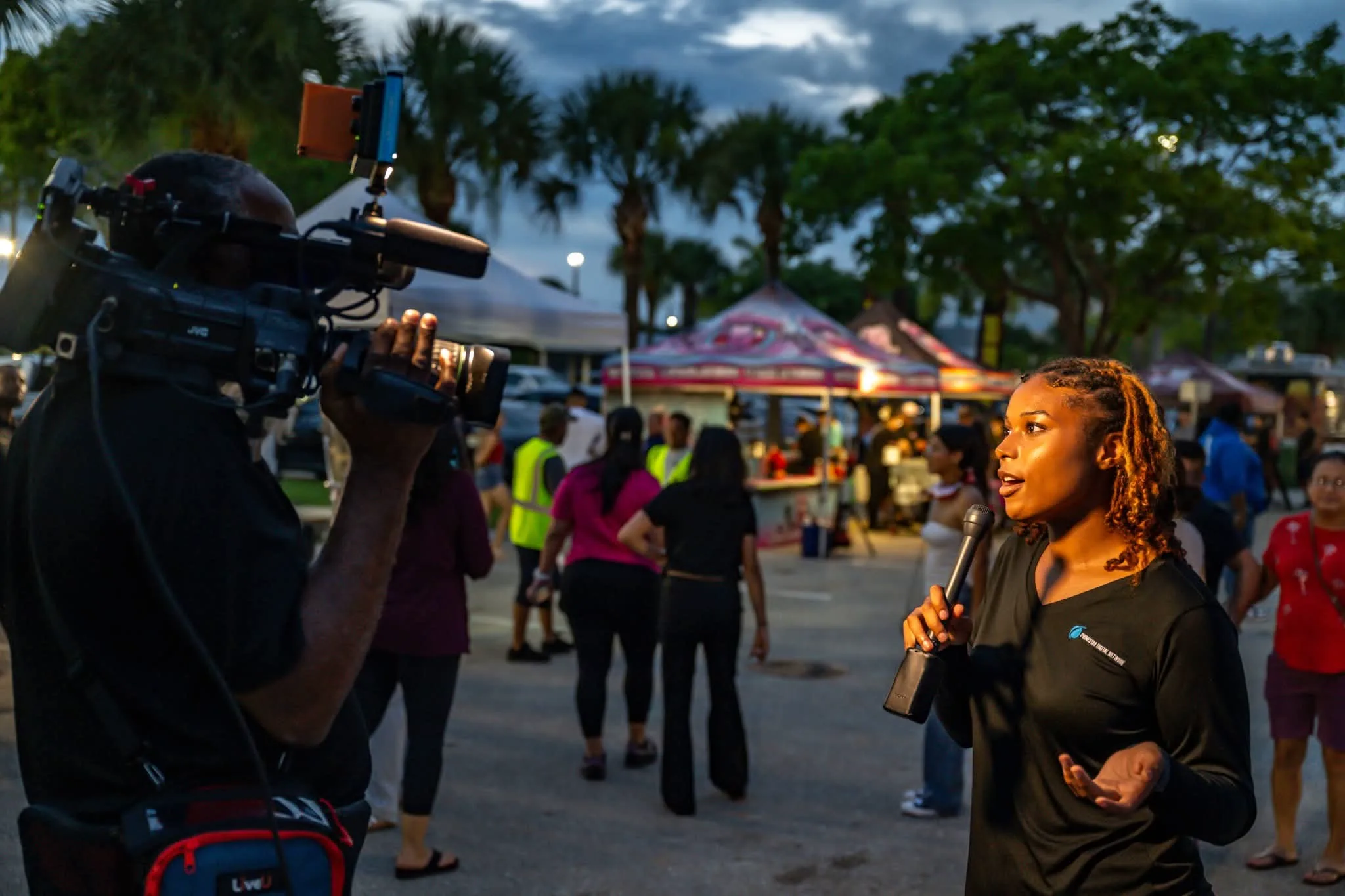 Primestar Digital Network field reporter on camera with a LiveU-equipped broadcast camera operator at a live outdoor event