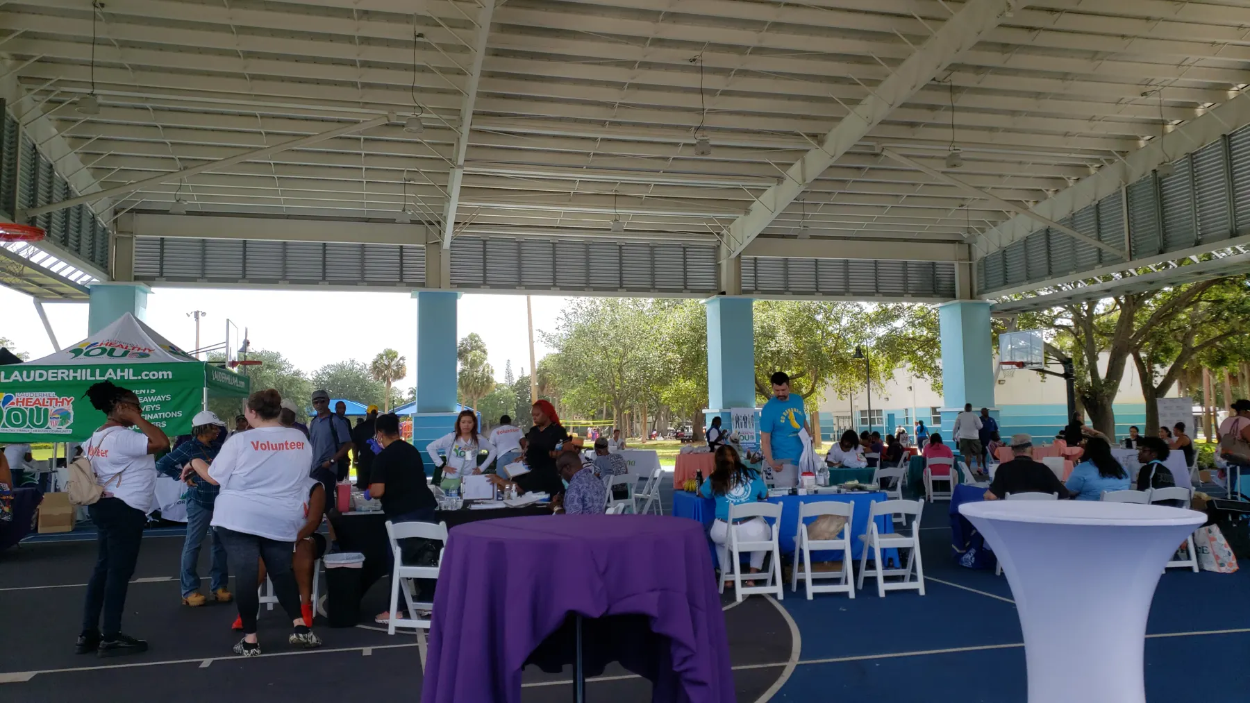 Health fair tables and visitors under the covered pavilion in Lauderhill